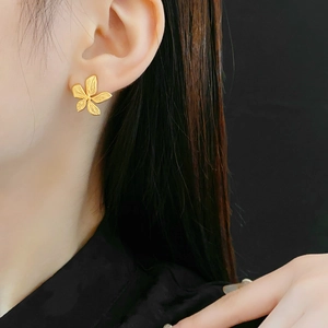Detail of gold floral stud earrings with a matte texture worn by a model on black background