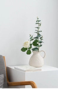 Detail of matte ceramic pitcher vase with elegant artificial white roses and greenery