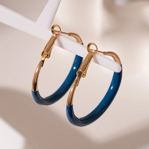 Detailed close-up of C-shaped golden metal hoop earrings with dark blue enamel coating