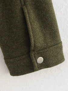 Détail du poignet d'une veste en laine vert foncé avec un bouton rond en métal argenté