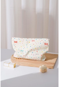 Detail of cream cotton makeup bag featuring colorful bow prints on a wooden tray