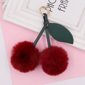Detail of plush cherry keychain with deep red fur balls and green leather leaves