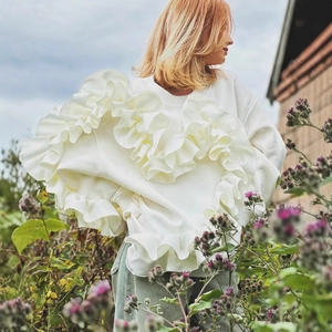 Dettaglio dell'elegante manica a balze su maglione lavorato a maglia bianco all'aperto
