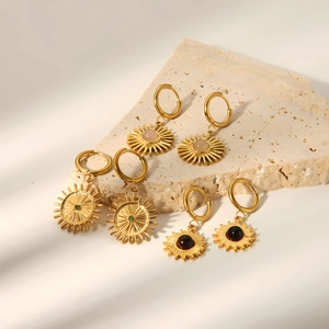 Gold plated sunburst hoop earrings with pink green and black stone insets on a stone