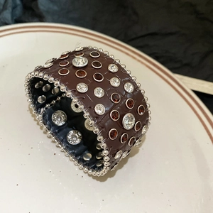 Détail d'un bracelet en cuir marron motif crocodile avec clous argentés et strass