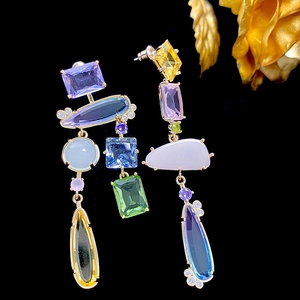 Macro detail of asymmetric drop earrings with multicolored crystals on black background
