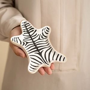 Zebra pattern ceramic jewelry tray with gold trim held by hand in soft natural lighting