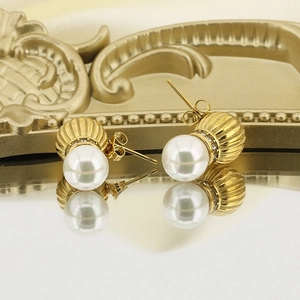 Vintage gold pearl stud earrings with textured base and crystal halo on reflective surface