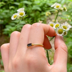 Detail of gold twisted rope ring featuring a rectangular black zircon worn in nature