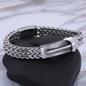 Detailed macro of stainless steel men's woven chain bracelet with engraved silver clasp