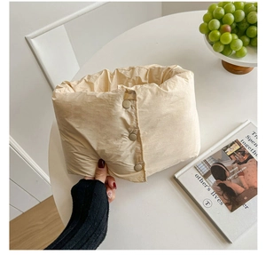 Dettaglio di sciarpa in piumino beige con chiusura a tre bottoni e trama soffice