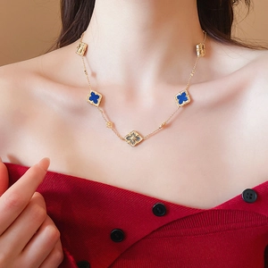 Close-up of gold plated necklace with blue clover pendants on a model wearing red top