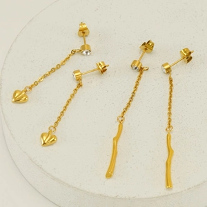 Golden heart and branch tassel earrings with rhinestones on a white pedestal stand