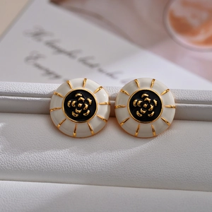 Elegant gold camellia flower earrings with black and white enamel on a white leather base