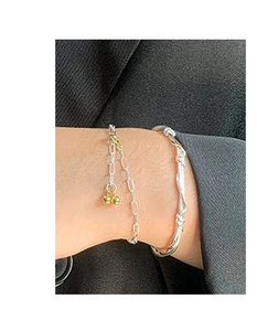 Detail view of woven silver bangle and gold bead bracelet on a black blazer sleeve