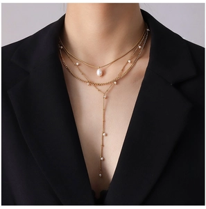 Detail of layered gold necklace with teardrop pearl and small beads on black suit