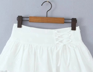 Detail of white mini skirt showing intricate floral embroidery and side lace-up bow