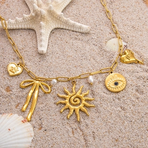 Golden tarot necklace with sun, angel heart and evil eye charms on textured sand