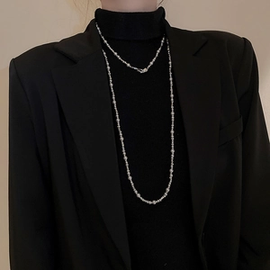 Détail d'un long collier à perles et pendentif lune argentée sur blazer noir