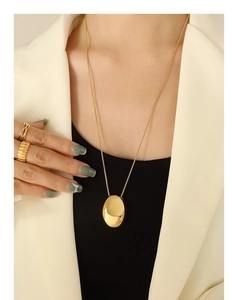 Détail d'un collier à pendentif ovale plaqué or minimaliste et de bagues texturées