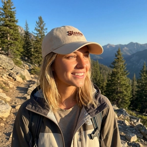 Beige cotton baseball cap with 'Since FASHION' embroidery shown in outdoor mountain scenery