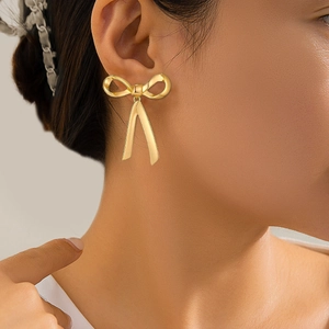 Close-up of golden bow-shaped V pendant earring worn by a model for a stylish look