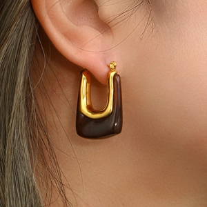 Close-up of a U-shaped gold metal and tortoiseshell acrylic earring worn on the ear