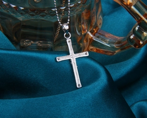 Gros plan d'un pendentif croix en argent s925 sur tissu en soie bleu canard avec chaîne à billes