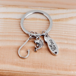 Detail of silver fish hook keychain engraved with Love You Dad on wooden background