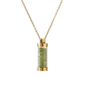 Close-up of golden necklace with cylindrical glass pendant filled with green crystals