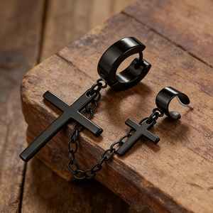 Macro detail of black stainless steel cross earring with chain and ear cuff on wood