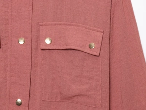 Detail of pink linen jacket featuring metallic gold snap buttons and cargo flap pocket