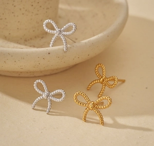 Detail view of gold and silver bow stud earrings with twisted rope texture on ceramic tray