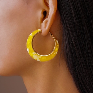 Close-up of C-shaped acetate hoop earring in yellow marble texture on female model