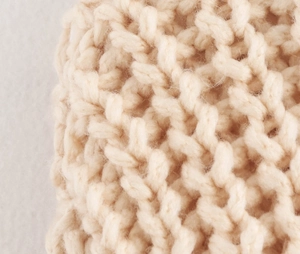 Macro shot of chunky V-stitch knit texture in beige, showing soft yarn fibers and warm detail