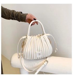 Detail of cream pleated bucket bag with gold-tone hardware and adjustable shoulder strap