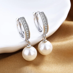 Détail macro de boucles d'oreilles perles en U argentées avec zircons sur porcelaine