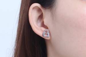 Macro shot of silver heart-shaped lock stud earrings worn by a model in soft lighting