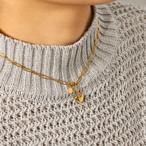 Gros plan du collier à pendentif cœur doré sur un pull en maille grise doux