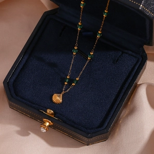 Detailed shot of golden shell pendant and green beads on a necklace in a velvet jewelry box