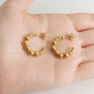 Close-up of gold beaded C-shape earrings on palm showing size and metal luster