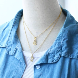 Close-up of layered gold initial necklaces with 'a' and 'G' pendants on a mannequin