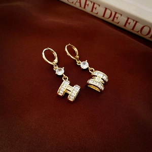 Close-up of gold-plated H-shaped earrings with sparkling cubic zirconia on brown satin