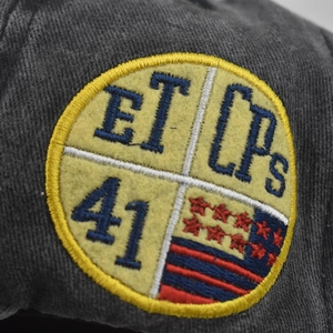 Macro shot of embroidered circular patch with ET and LPs lettering on dark grey cap