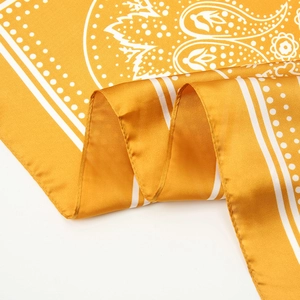 Detailed view of the bright yellow paisley silk scarf showing the smooth satin texture