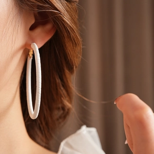 Close-up of a white leather geometric hoop earring worn by a model in a natural setting