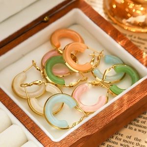 Detailed macro view of colorful macaron resin C-shaped gold-plated hoop earrings in a wooden box