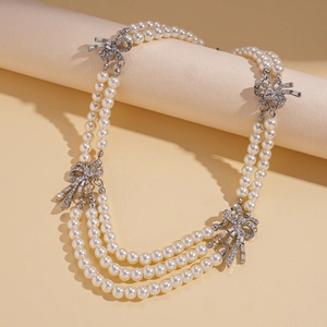 Macro shot of three-layer faux pearl necklace with rhinestone-studded silver bow detail