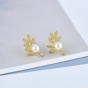 Elegant gold leaf earrings with white pearls and sparkling crystals on a gray background