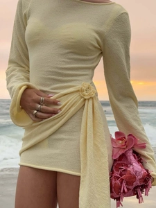 Detail of knit mini dress with handmade crochet flower and wrap waist at sunset beach